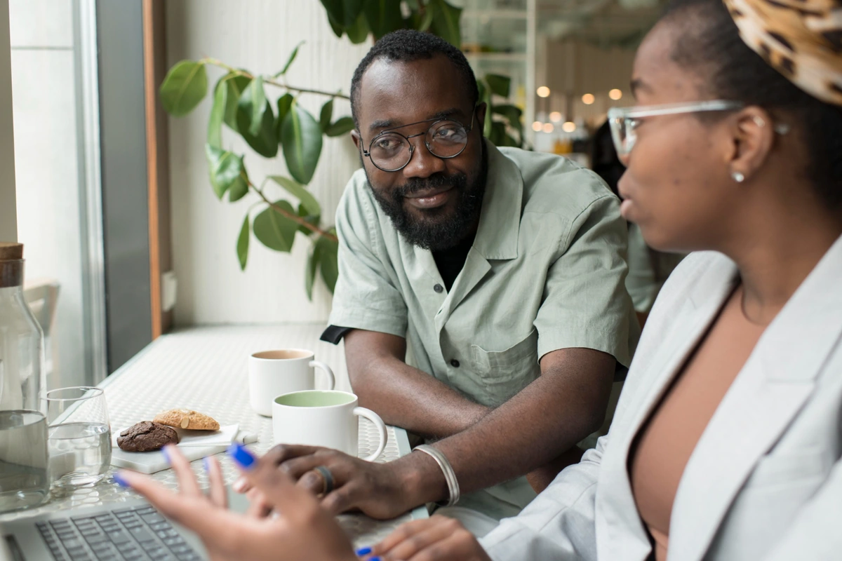 Illustrative scene: two people talking beside a laptop.